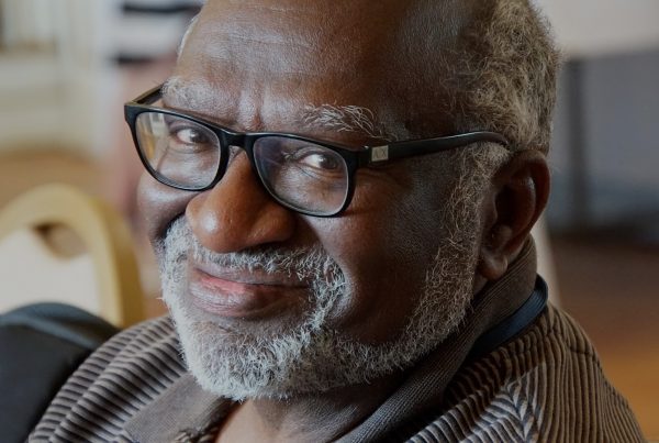 Charles Coe headshot for poetry reading event. Black man with glasses and facial hair close up smiling.